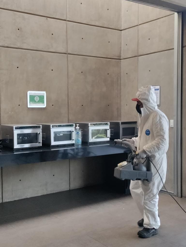 Técnico aplicando fumigación profesional en área de cocina corporativa con equipo especializado y medidas de bioseguridad.