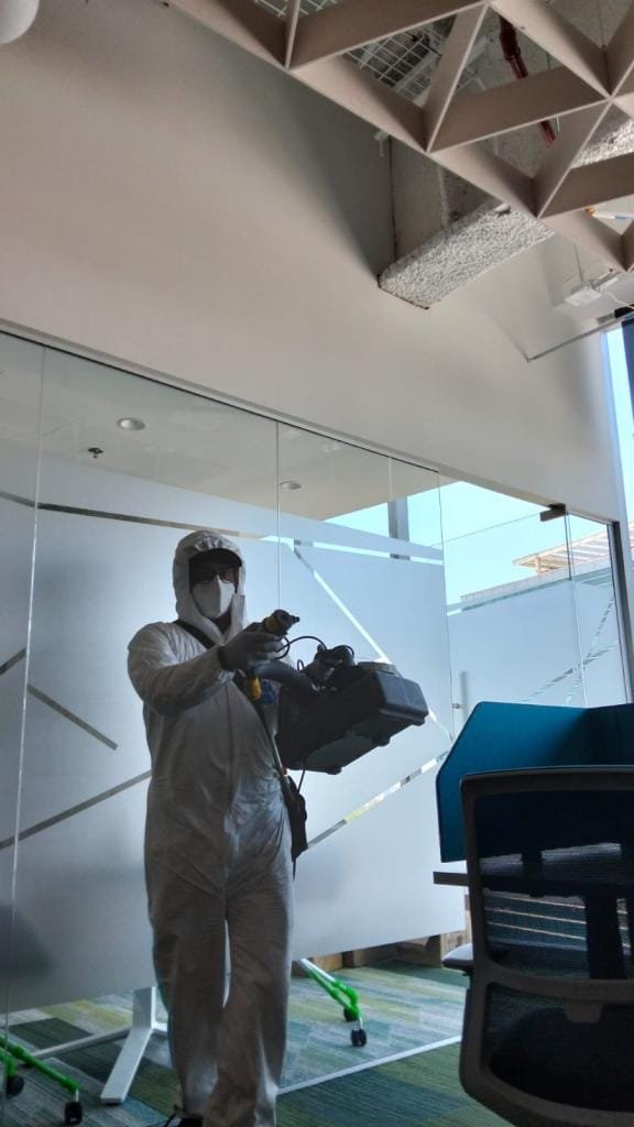 Técnico aplicando fumigación profesional en oficinas modernas con equipo especializado de nebulización.