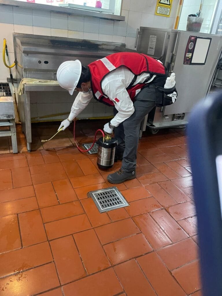 Técnico profesional aplicando fumigación en cocina industrial con equipo especializado.