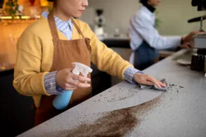 Mujer limpiando encimera sucia en un negocio de alimentos para mantener condiciones higiénicas y prevenir plagas.